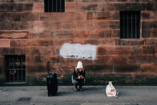 Woman texting on kerb with cellphone and luggage, Edinburgh, Scotland