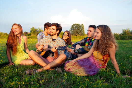 Group of young adults sitting in field listening to acoustic guitar