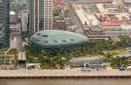 Shanghai, China - May 4, 2010: Green Tear-shaped Glass Cruise Terminal Building In Green Park Set Along Brown Water River With Buildings In Back.