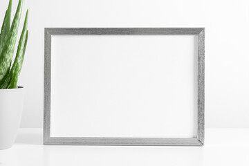Gray frame mockup with workspace accessories and aloe vera on white table. Front view. Place for...