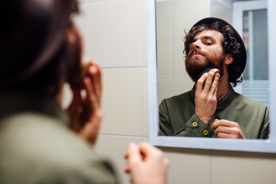 Bearded young man brushing beard in bathroom