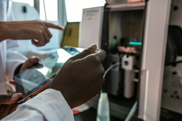 Young female and male scientists using digital tablet and scientific equipment in laboratory, cropped