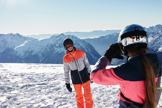 Teenage girl skier taking photo of teenage brother on snow covered mountain top,  Alpe-d'Huez, Rhone-Alpes, France