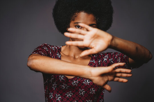 Young woman with afro hair covering face with hands, grey background