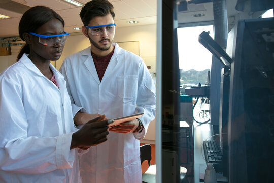 Young female and male scientists looking at scientific equipment in laboratory