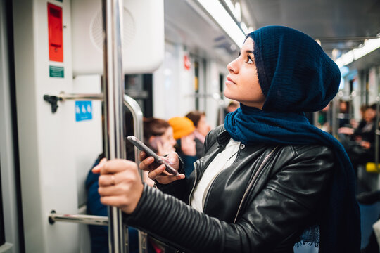 Young woman in hijab with smartphone on subway train