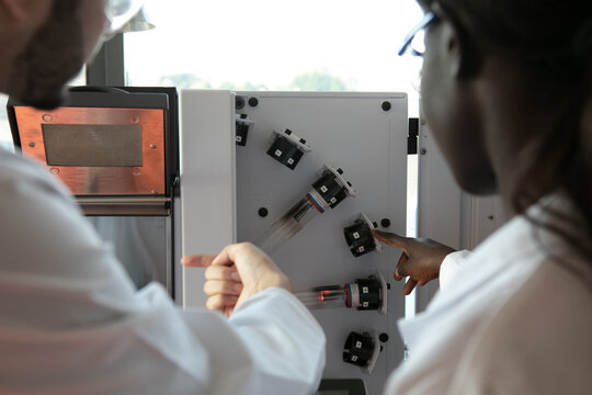 Young female and male scientists looking at scientific equipment in laboratory, over shoulder view - Powered by Adobe