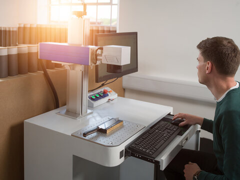 Knife factory worker using computer keyboard to operate laser cutting equipment in workshop