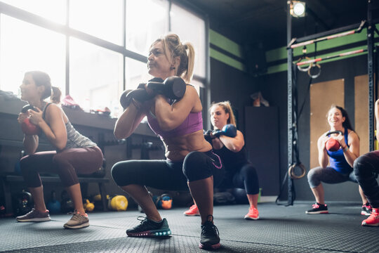 Women training in gym, squatting with kettle bells