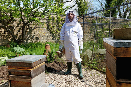 Male beekeeper carrying bee smoker in walled garden, portrait
