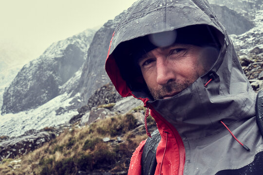 Male hiker with hood up in sleeting snow capped mountain landscape, close up portrait, Llanberis, Gwynedd, Wales