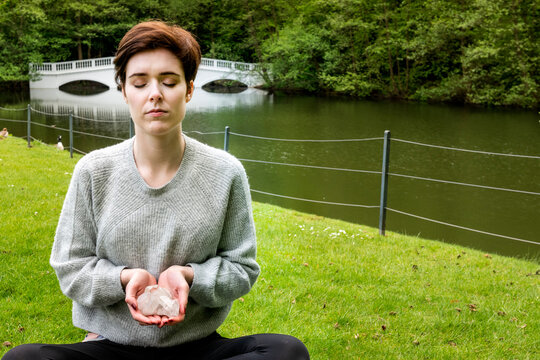 Woman practising Reiki on grass lawn by river, London, UK