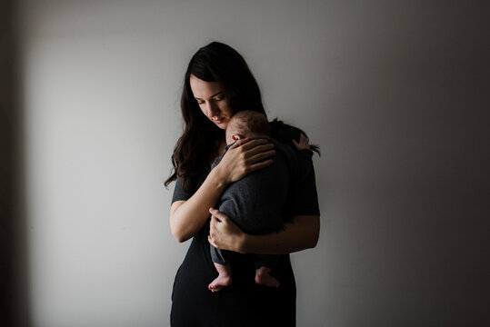 Young woman carrying baby son in arms, low key