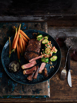 Rustic low key still life with plate of rubbed steak and spiced brussels sprouts on table, overhead view