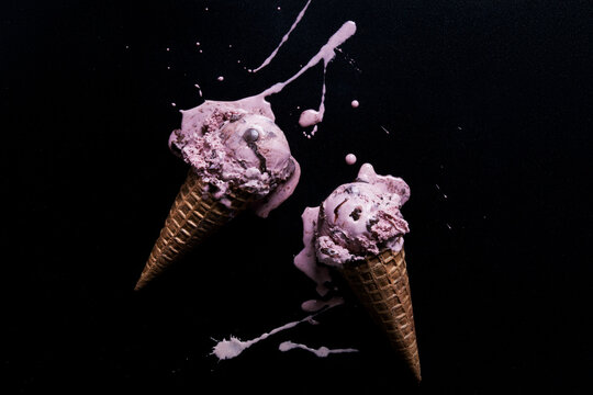 Two chocolate chip raspberry ice-cream cones with melted splash against black background, overhead view