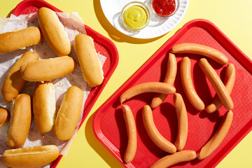 Tray of bread finger rolls and tray of hotdogs on yellow background