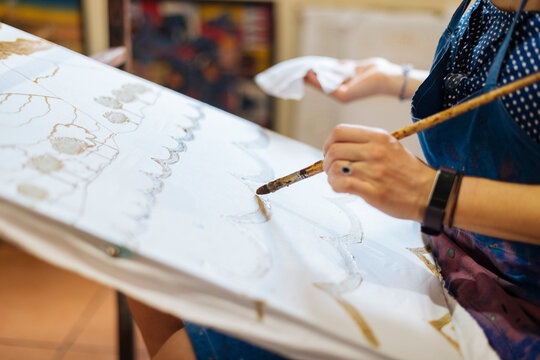 Young woman practicing Batik in art classroom, a traditional form of Indonesian painting, cropped view of hands
