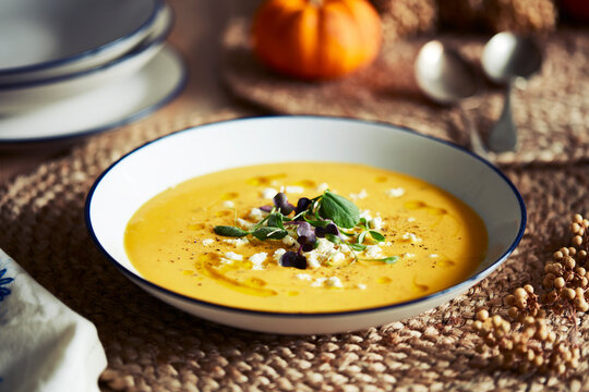 High angle close up of bowl of pumpkin soup with garnish on rustic place mat.