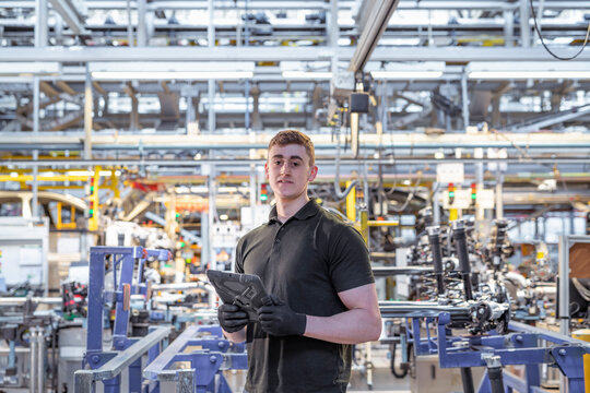 Portrait of apprentice engineer with digital tablet in car factory