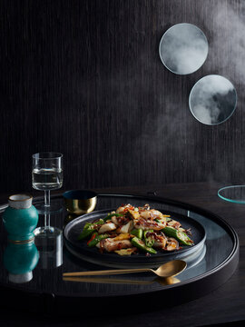 Rustic low key still life with plate of stir fry coral trout, okra and xo sauce on tray