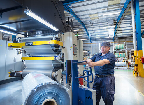 Worker moving rolls of food packaging material in print factory
