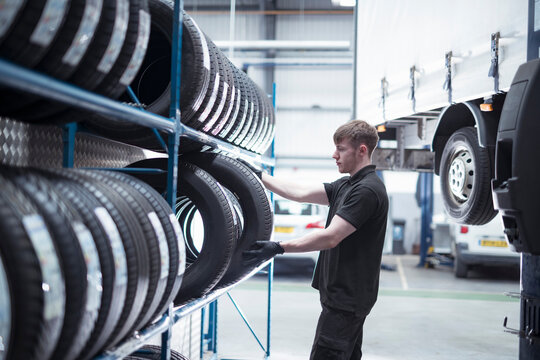 Apprentice Engineer Selecting Tyres In Car Service Centre 