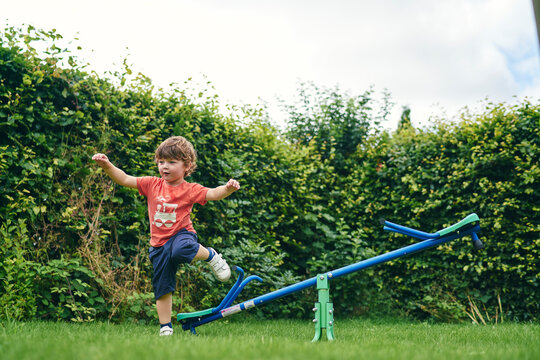 Boy hopping off toy seesaw in garden