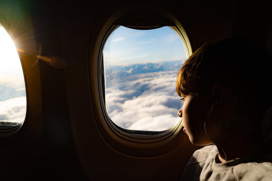Teenage boy looking out through airplane window at clouds on airplane journey