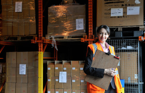Young female factory worker with clipboard in warehouse, portrait