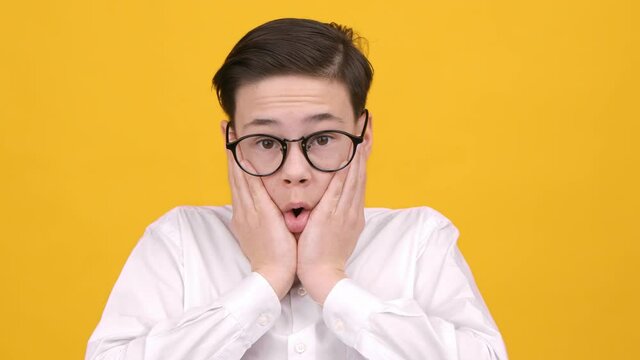 Shocked Teen Boy Looking At Camera Touching Face, Yellow Background