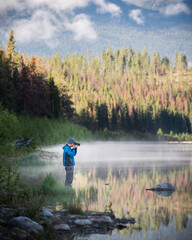 Fototapeta na wymiar A photographer in a blue jacket lines up his shot along a bright and sunny morning in Jasper National Park.