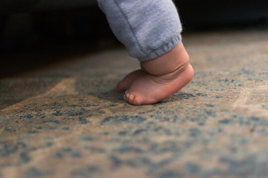 9 month old baby learning to pull up, cruise, and walk; leaning against side of couch - closeup of feet