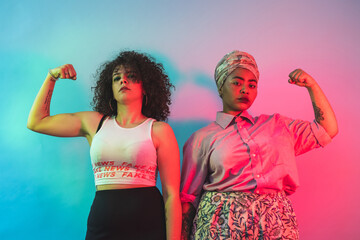 Young women flexing arms against blue and pink background