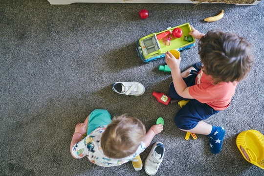  Boys Playing With Toy Trucks And Assorted Toys On Rug