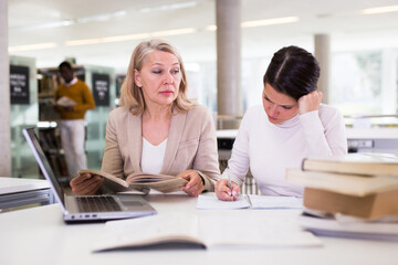 Fototapeta premium Female teacher working with girl student in university library. High quality photo