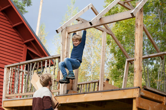 Father watching boy swinging on beam of unfinished treehouse