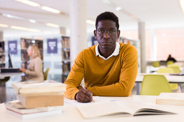 Portrait of confident african-american male student working with book in public library. High quality photo