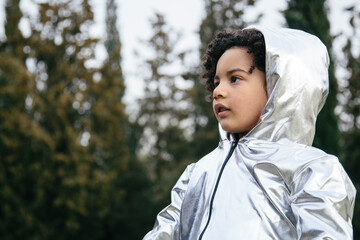 Black boy wearing a silver clothing, looking away. In a park background. Copyspace. Kids, astronauts, extraterrestrials and black people concept