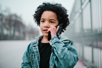 Fototapeta na wymiar Afro child talking on his mobile phone. In a courts background. Kids, smartphones and black people concept.