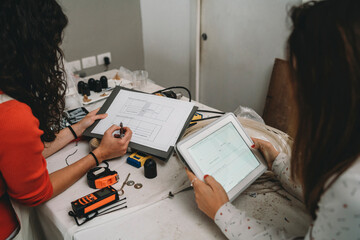 Two mid adult women looking at plans and digital tablet in their new shop, over shoulder view