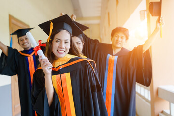 The Asian university graduates in graduation gown and a mortarboard cap with a degree certificate...