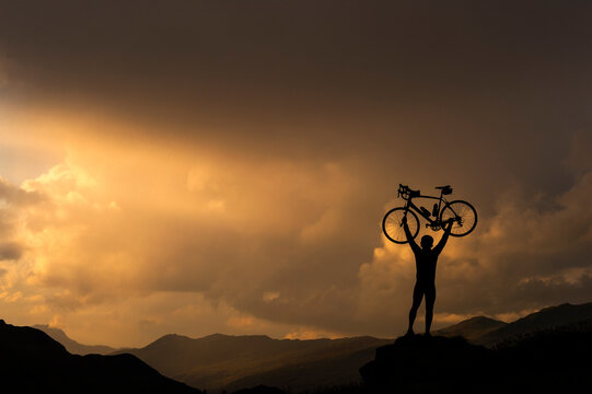 Cyclist lifting bicycle against sunset on hill