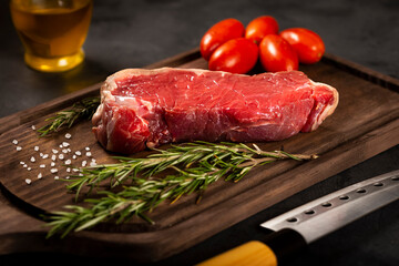 Fresh raw steak on wooden board on a dark background with salt, tomatoes and rosemary.