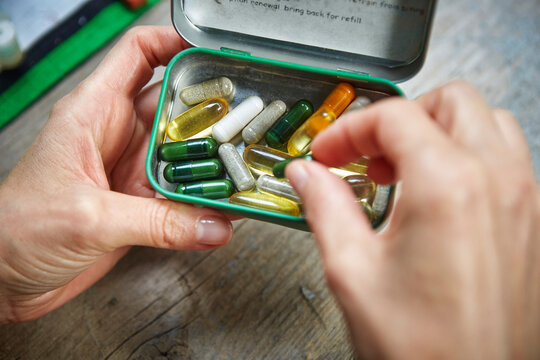 Person picking up capsule from pillbox held in hand