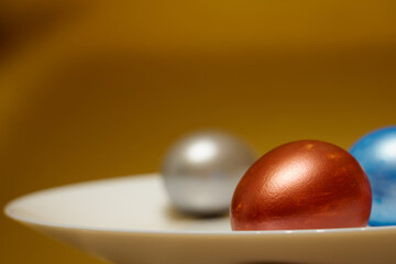 Painted eggs on a white plate with golden background.