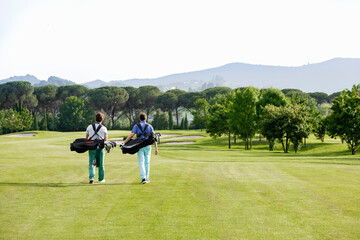 Friends carrying golf bag walking on golf course