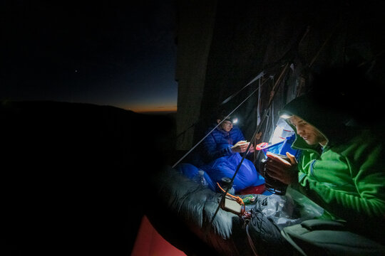 Two mountaineers in a portaledge at night, reading with flashlight, El Capitan, Yosemite National Park.