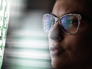 Female data analyst looking at data on screen, reflection in glasses.