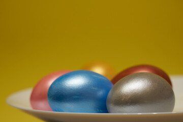 Painted eggs on a white plate with a yellow background.