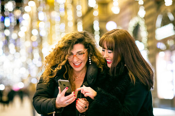 Two women smiling and looking at a mobile phone in a Florence street.